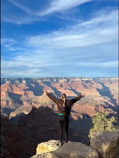 Fachkraft steht mit ausgebreiteten Armen am Grand Canyon